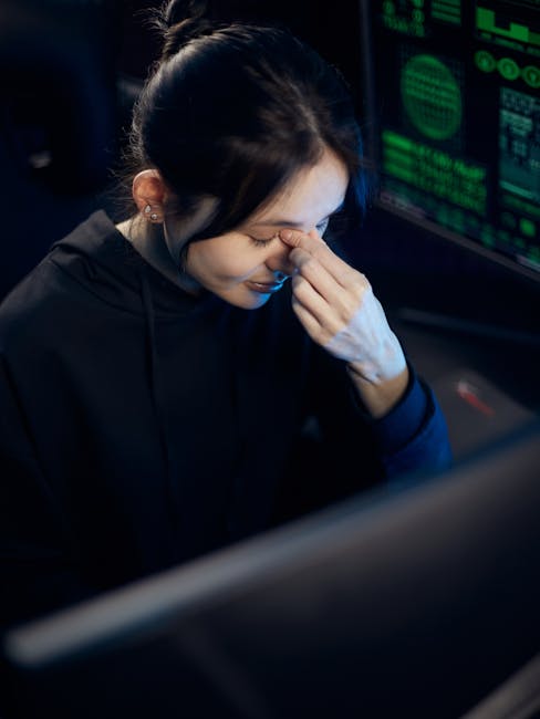 Tired office worker rubbing dry irritated red eyes while working at computer screen in dry indoor environment showing symptoms of digital eye strain and dry air exposure